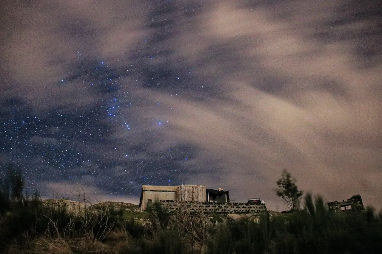 Estrellas entre nubes con una ruina en primer plano