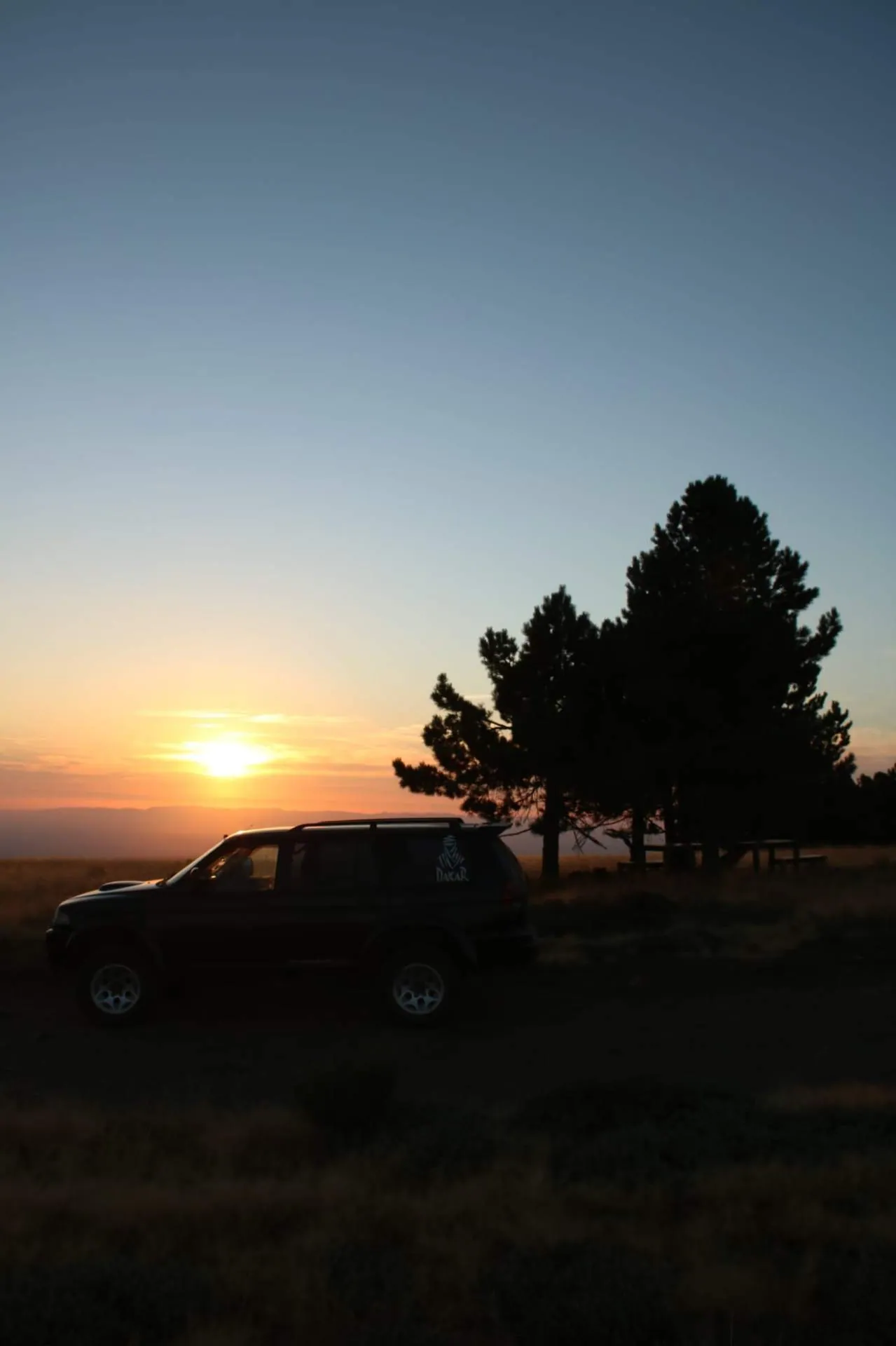Jipe 4x4 junto a árvore solitária ao pôr do sol